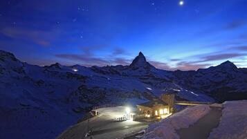 A snow-covered mountain landscape at night with a lit building and a clear view of a mountain peak.