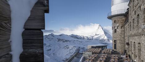 A snow-covered mountain with a restaurant terrace and a stone building with a dome.