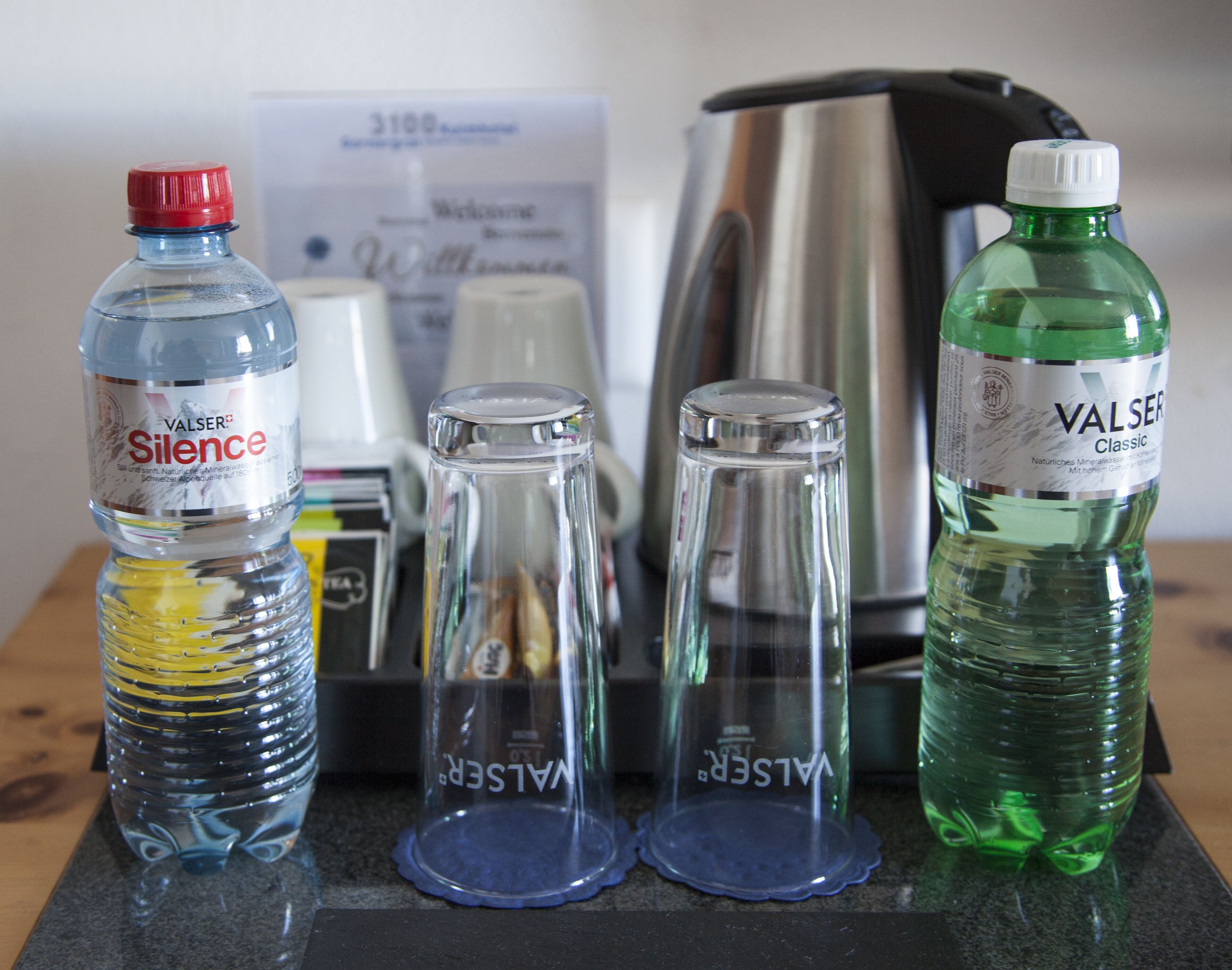 Three water bottles and two empty glass containers on a countertop.
