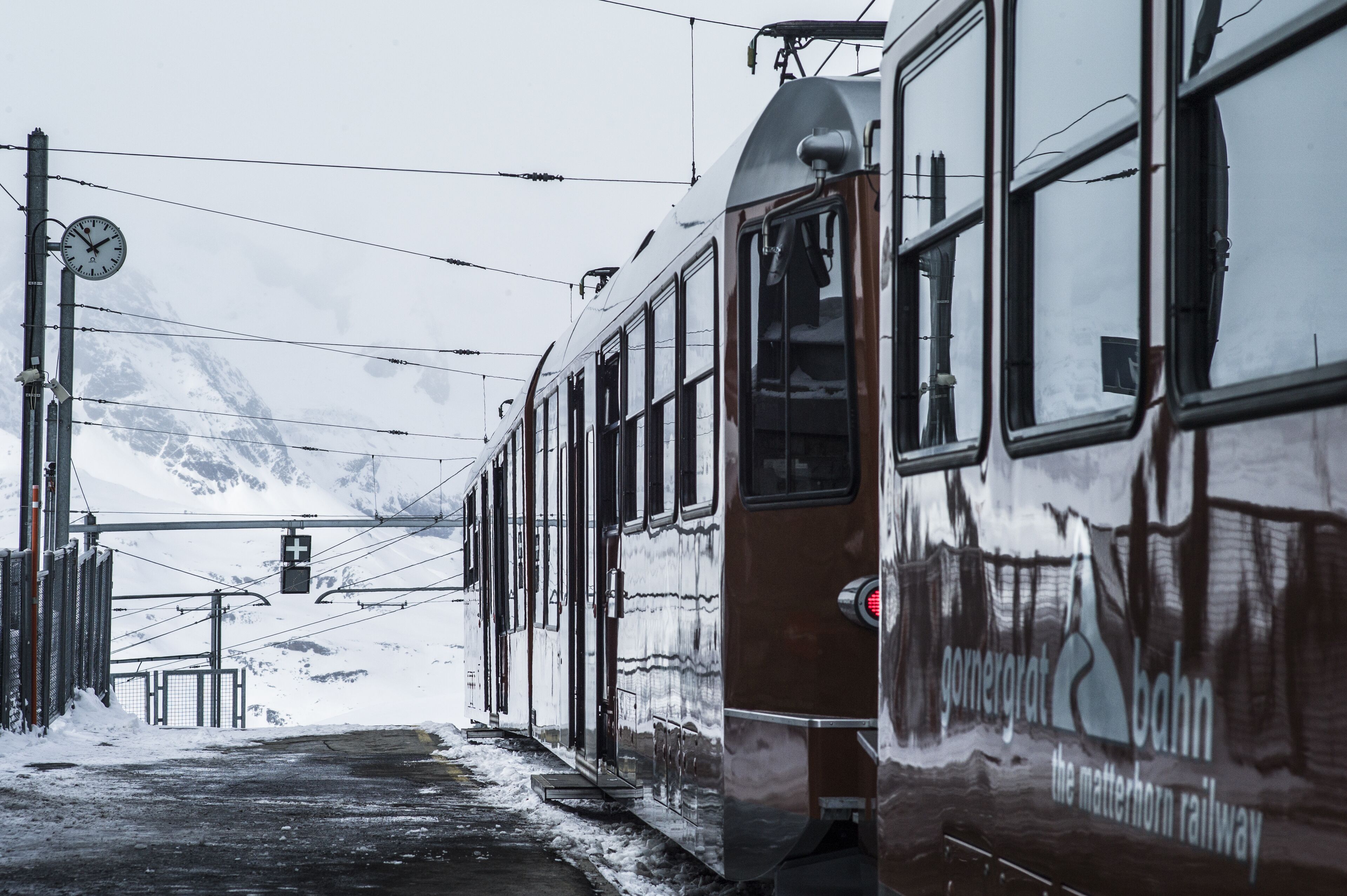 Un tren en una estación con una montaña nevada al fondo.