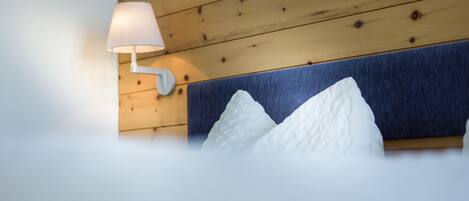 A hotel room with a wooden headboard, a wall-mounted lamp, and two white pillows.