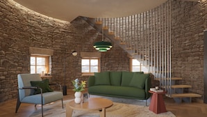 A cozy living room with a stone wall, a green sofa, a wooden coffee table, and a staircase with a metal railing. - 3100 Kulmhotel Gornergrat (Zermatt)