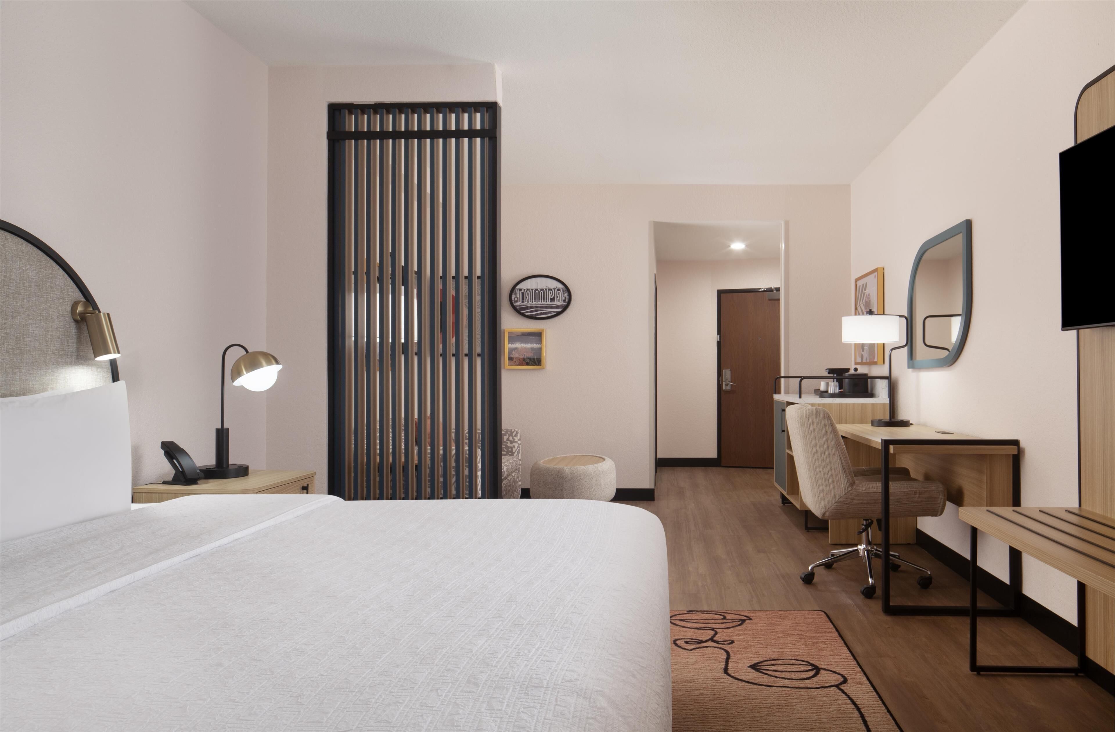 Een hotelkamer met een bed, bureau, stoel, lamp en een schuifdeur.