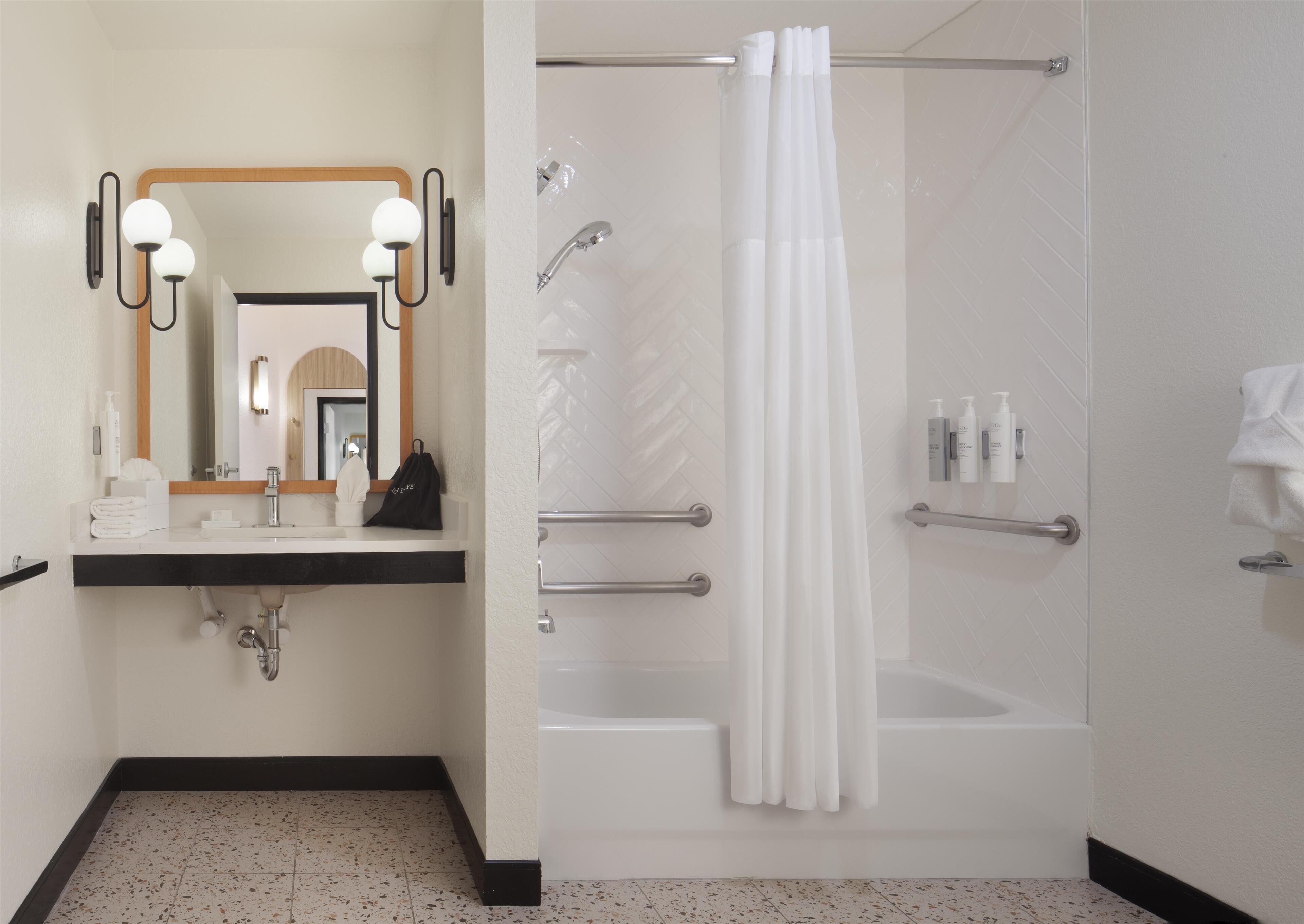 A modern bathroom with a sink, mirror, towel rack, shower, and toiletries.