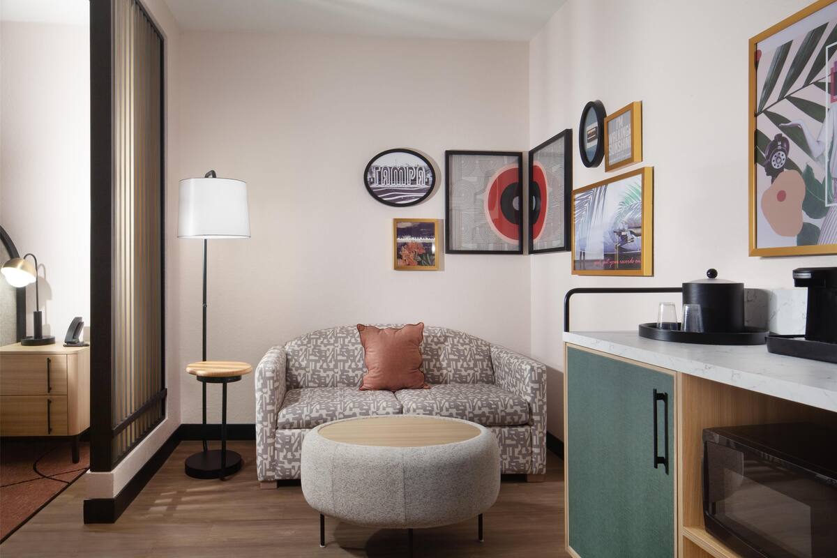 Ein modernes Wohnzimmer mit Sofa, Hocker und Couchtisch. Eine Lampe, eine Mikrowelle und ein Schrank sind ebenfalls vorhanden.