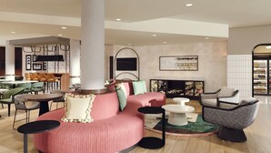 A modern lounge area with a round pink sofa, green and white chairs, a white coffee table, and a fireplace.
