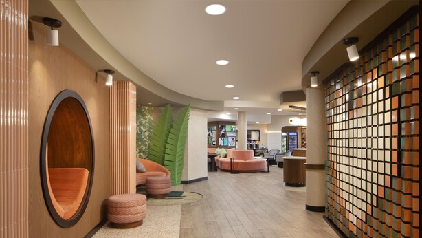 A modern lobby with a curved ceiling, wooden accents, and a seating area with orange and patterned ottomans.