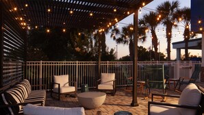 An outdoor patio with seating, string lights, and palm trees.