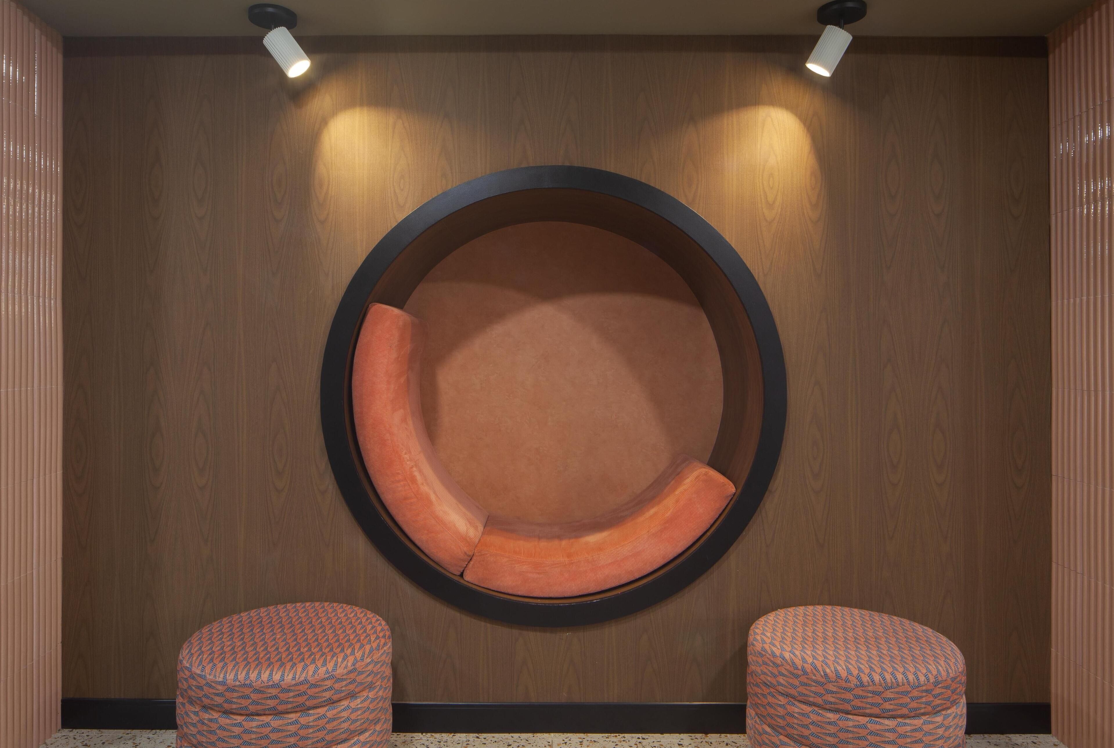 Un espace de détente circulaire, avec un mur en bois servant de fond et deux poufs à motifs.