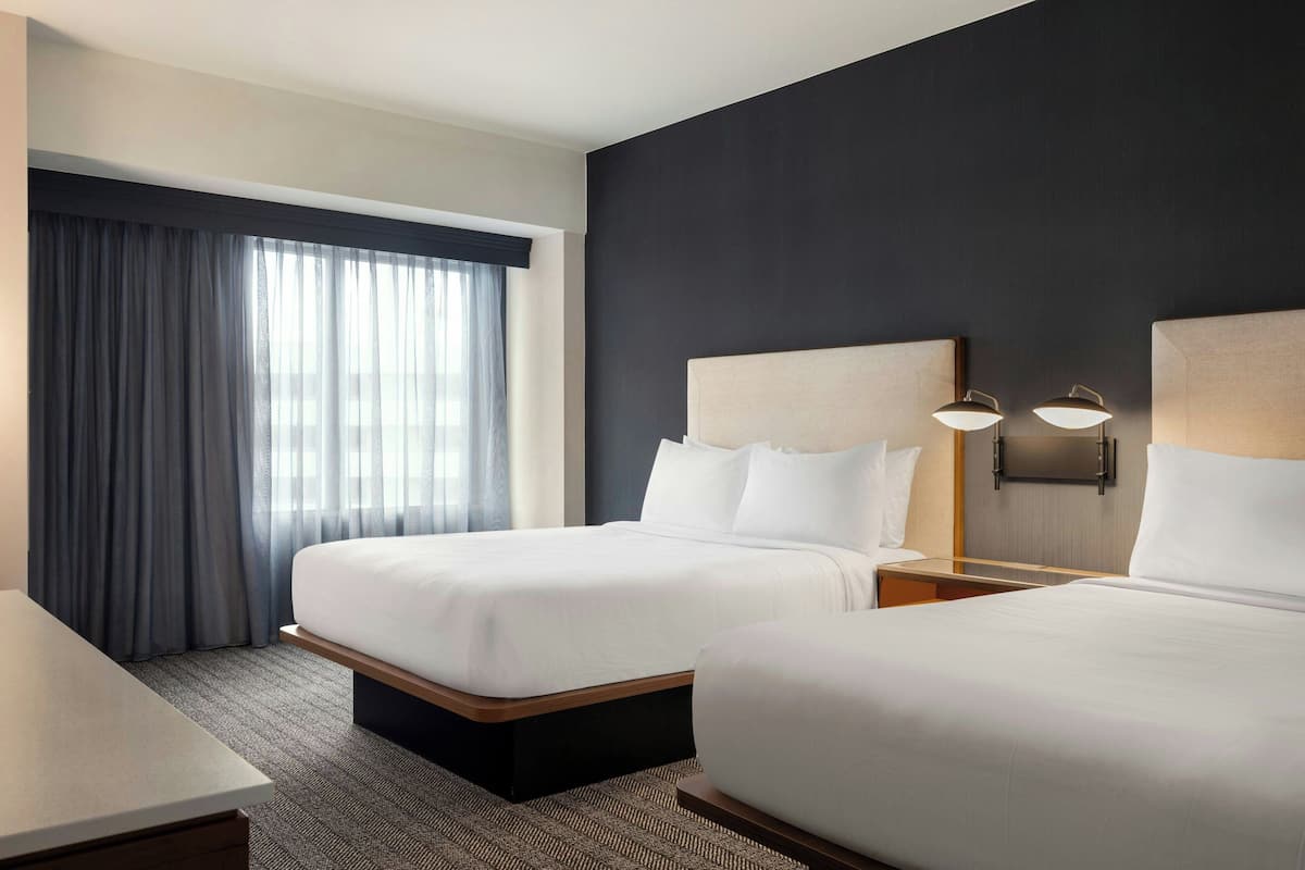 Una habitación de hotel con dos camas, un escritorio y un ventanal con cortinas.