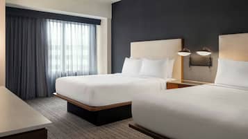 Ein Hotelzimmer mit zwei Betten, einem Schreibtisch und einem großen Fenster mit Vorhängen.