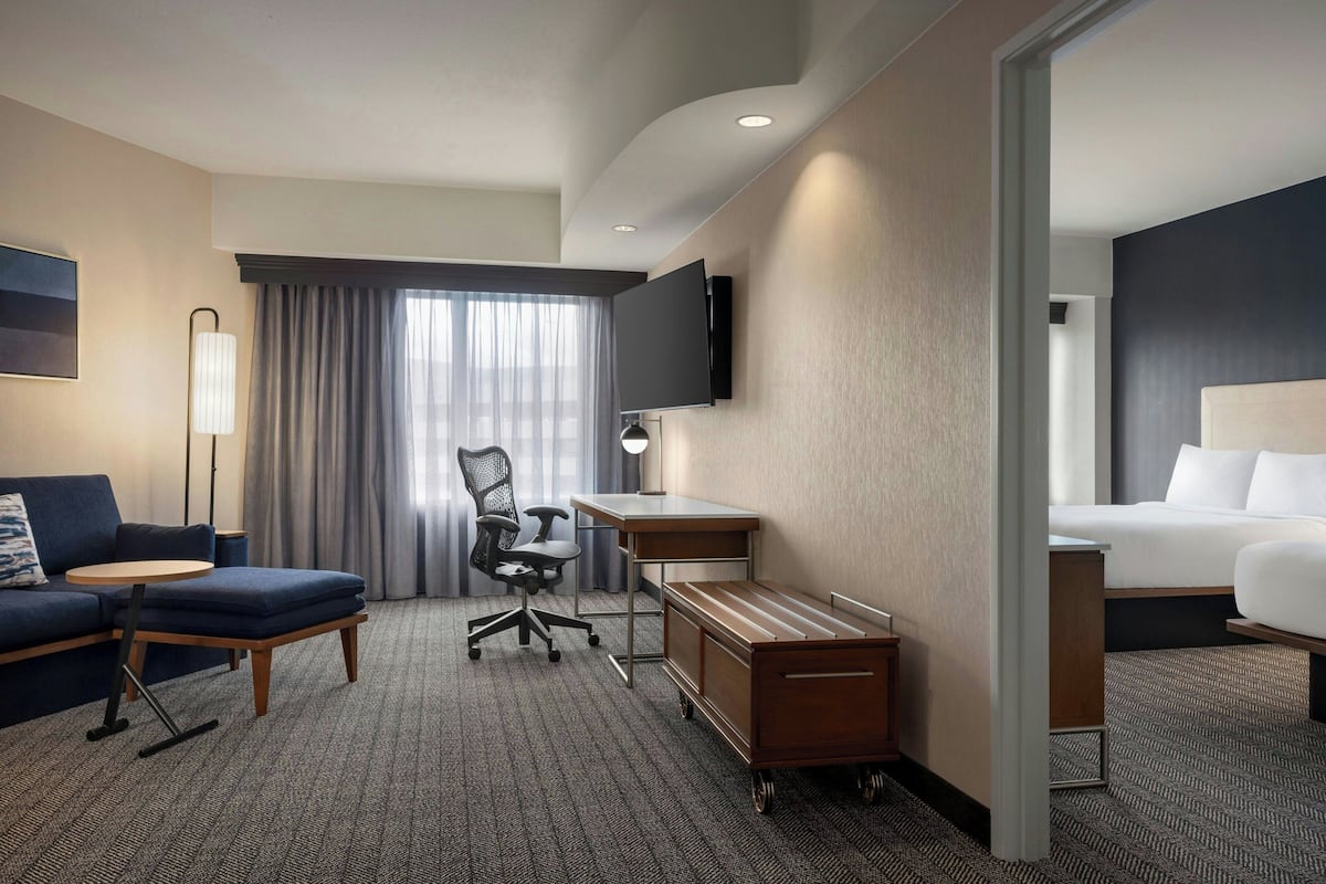Ein Hotelzimmer mit einer Couch, einem Schreibtisch, einem Stuhl, einem Fernseher, einem Bett und einem Rollwagen.