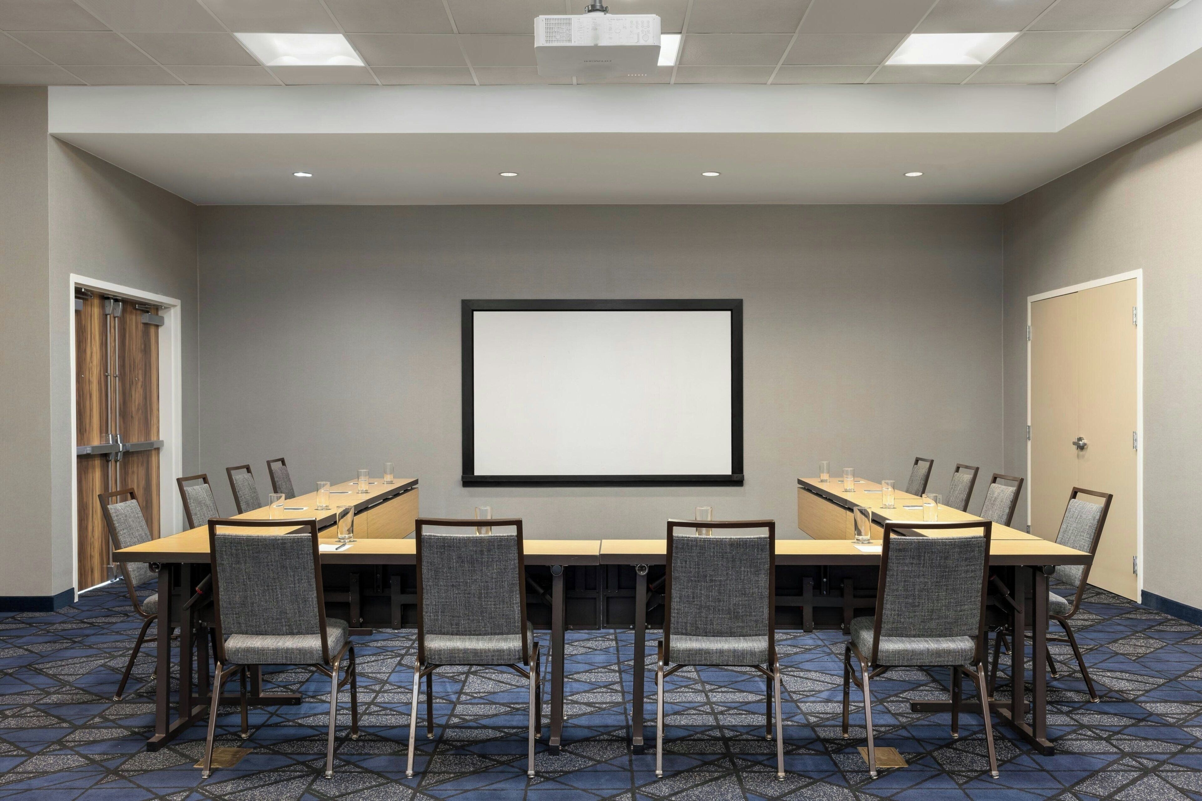 A conference room with a long table, chairs, a projector screen, and a door.