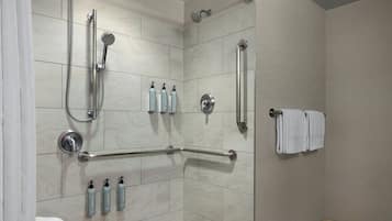 A shower with a grab bar, a towel rack, and toiletries on the wall.