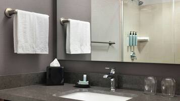 A bathroom with a sink, two towels, a mirror, a glass shower enclosure, and toiletries.
