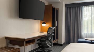 A hotel room with a desk, chair, bed, TV, and a window with curtains.