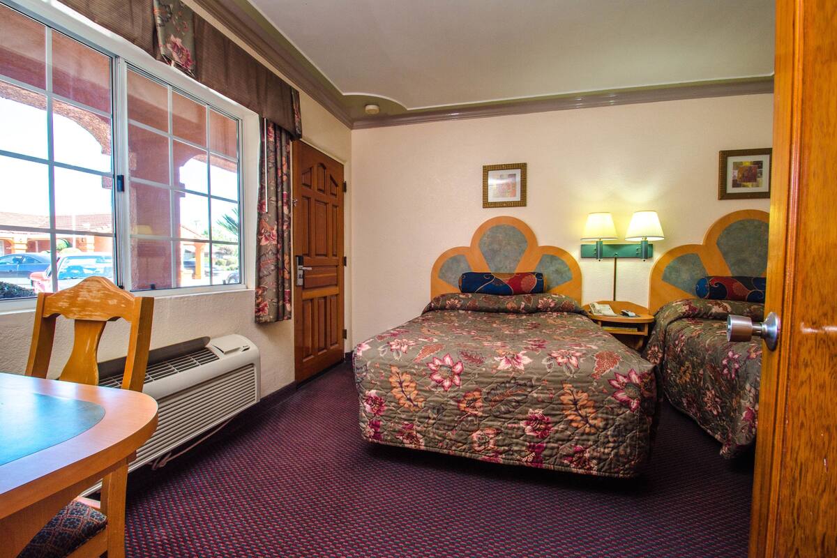 A hotel room with a large window, a bed with floral bedding, a desk, and a chair.