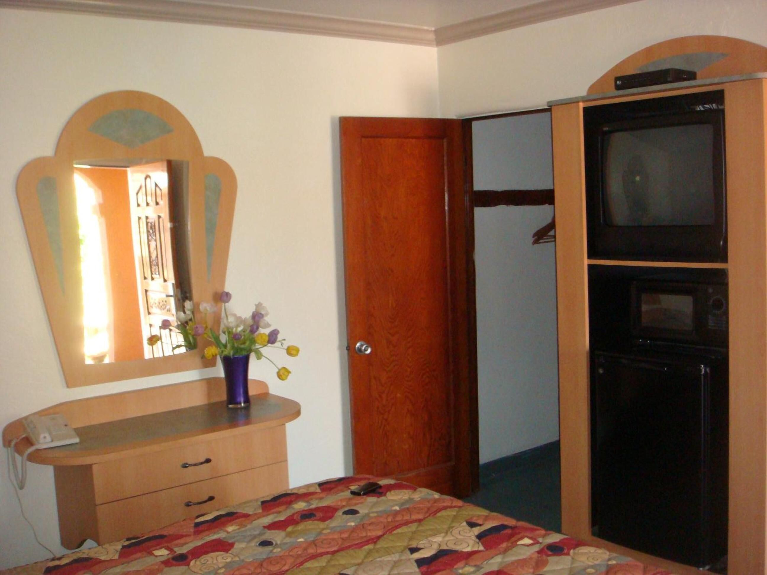 A bedroom with a bed, dresser, mirror, and a wardrobe with a television.