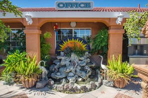 An office building with a sign, a decorative sun, and a rock fountain.