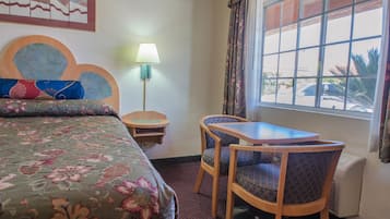 A hotel room with a bed, a table, two chairs, a lamp, and a window with a view of the outside.