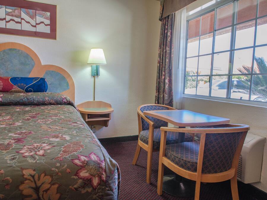 A hotel room with a bed, a table, two chairs, a lamp, and a window with a view of the outside.