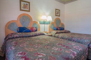A double bed with floral bedding, a nightstand, two wall-mounted lamps, and two framed pictures on the wall.