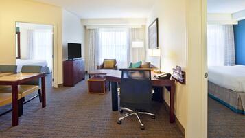 A hotel room with a bed, a desk with a chair, a television, and a desk lamp.