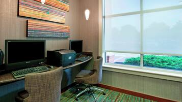 Habitación de hotel con escritorio, dos monitores, una impresora y un amplio ventanal con vistas a zonas verdes.