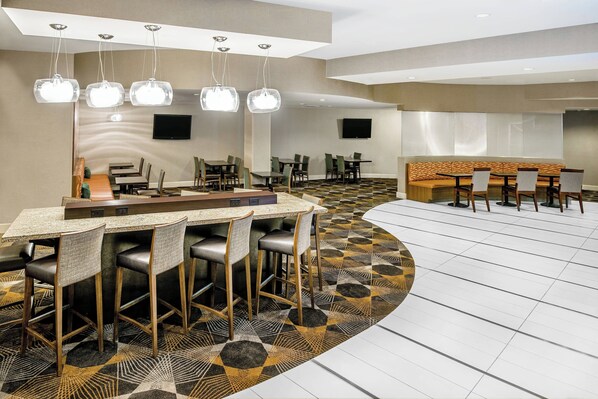 Un hall de hotel con una zona de bar central, diversas opciones de asiento y un suelo estampado.