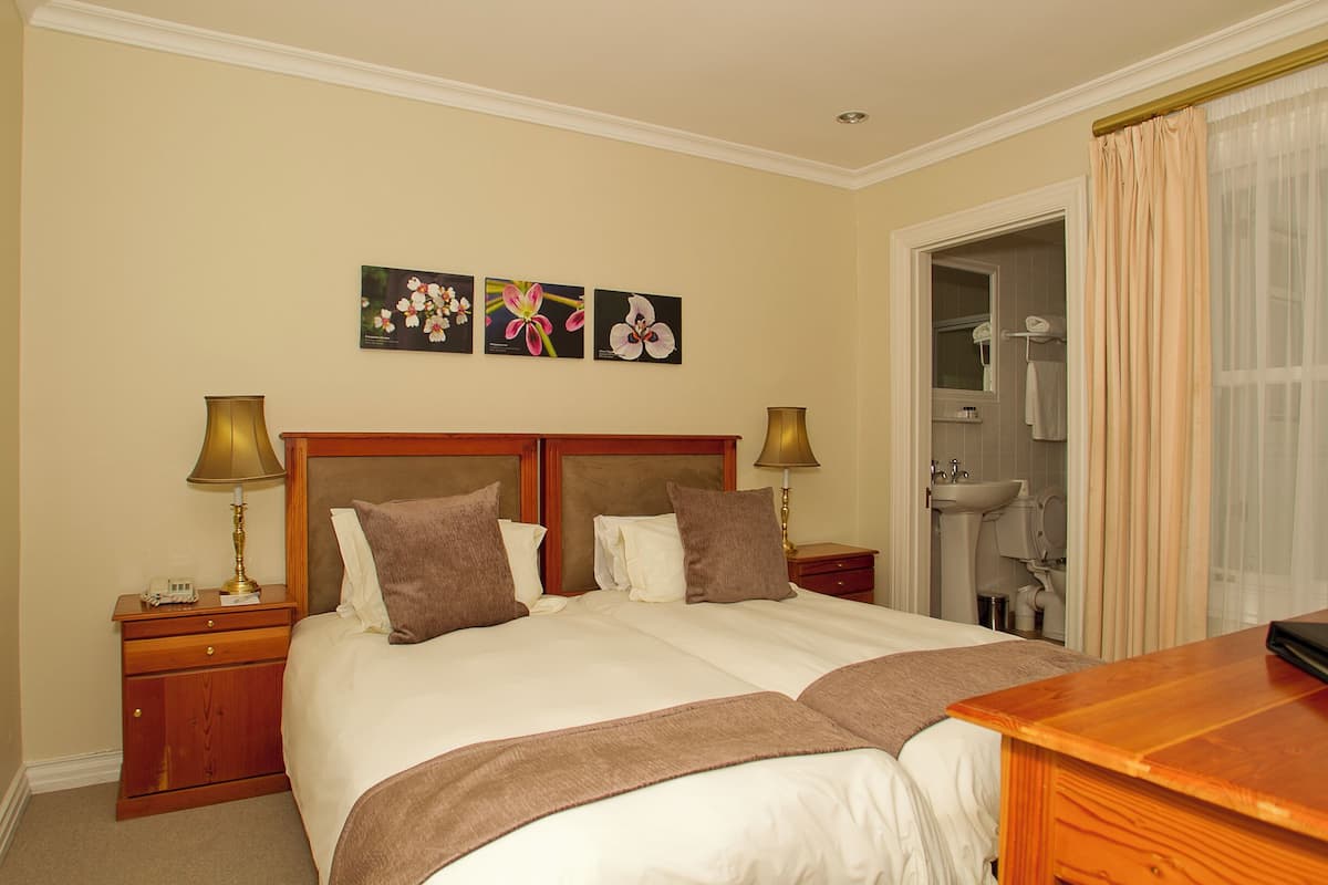 A hotel room with a double bed, two bedside tables, a nightstand, a desk, a chair, a mirror, a sink, and a shower area.