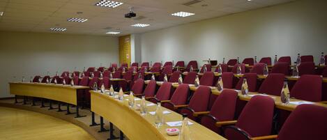 Un salón de conferencias con filas de sillas rojas y una mesa de madera larga.