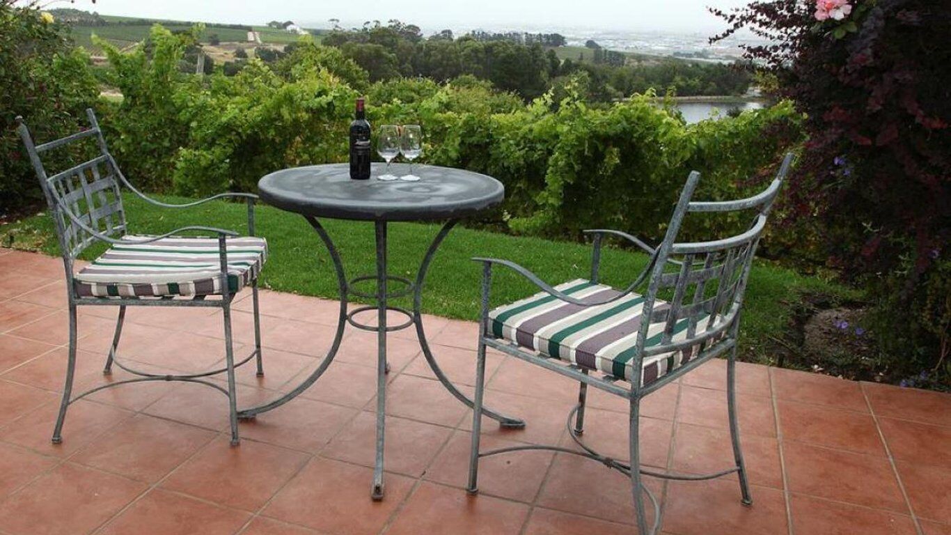 An outdoor patio with two metal chairs and a table, a bottle of wine, and two glasses on the table.