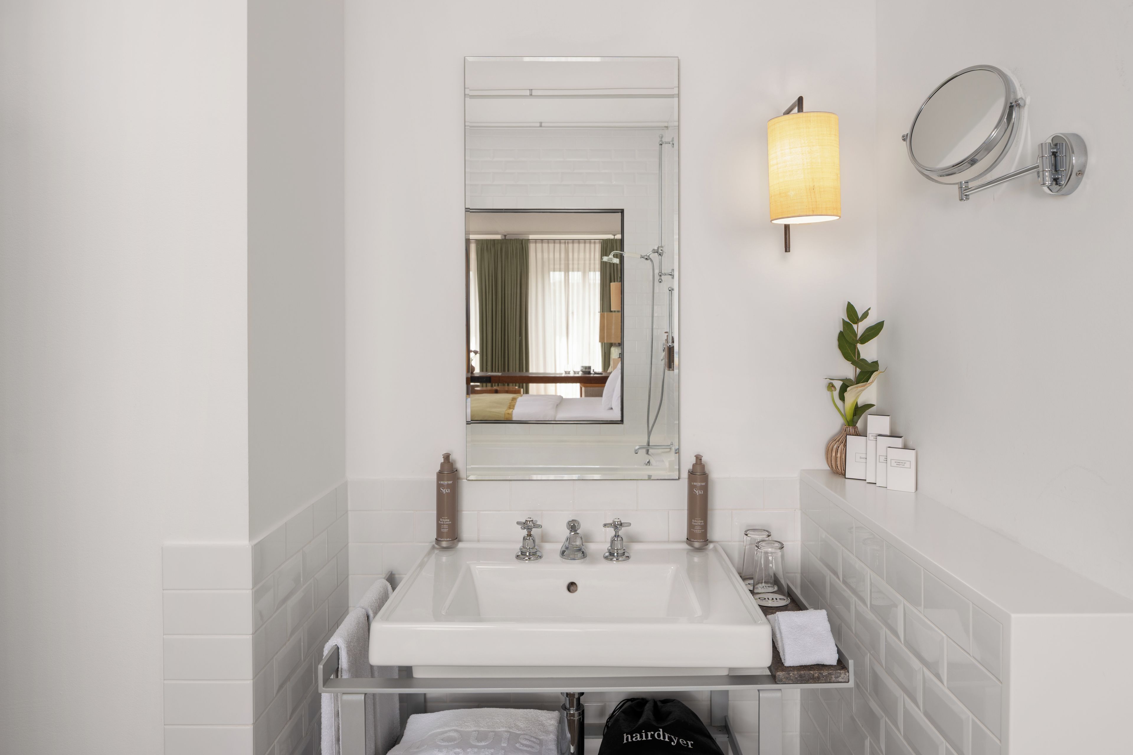 A modern bathroom with a large mirror, two sinks, a shower, and a towel rack.