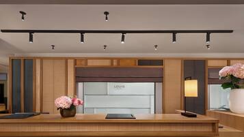 A hotel reception desk with a modern design, a nameplate, a vase with flowers, and a lamp.