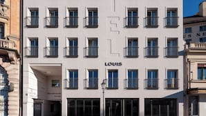 Un moderno edificio de hotel con fachada blanca, varios balcones y un llamativo letrero 'LOUIS' en la planta baja.