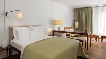 A hotel room with a bed, bedside table, desk, chair, and a view of a curtain.