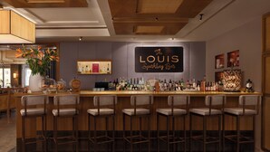 Zona de bar con un letrero que dice 'The Louis Sparkling Bar', taburetes y una variedad de botellas y vasos sobre la barra.