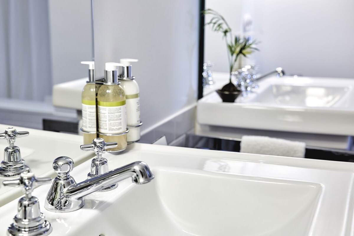 A bathroom with a white sink, chrome faucets, and two bottles of liquid soap.