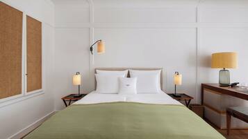 Quarto de hotel com uma cama, duas mesas de cabeceira, um criado-mudo, uma luminária e uma cesta de vime.