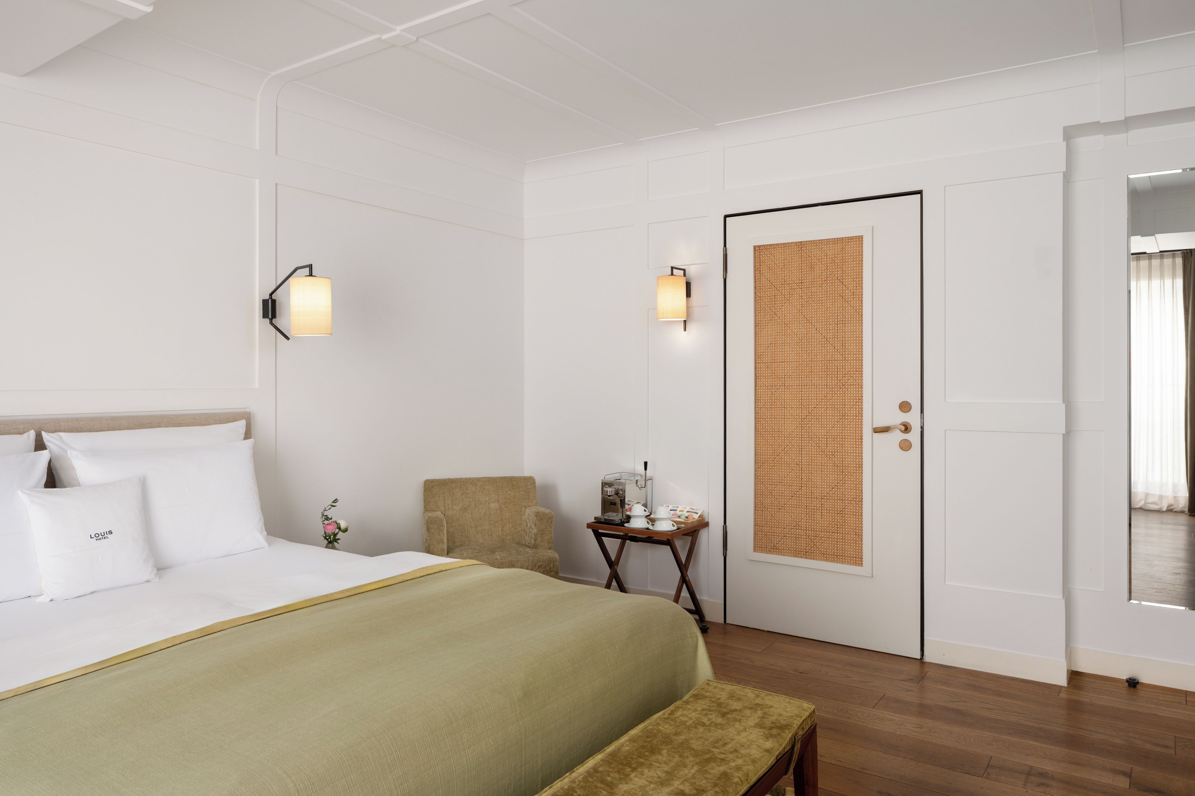 Ein Hotelzimmer mit einem Bett, einem Sessel, einem kleinen Tisch mit Kaffeemaschine und einer Tür mit einem Gewebeshobfenster.