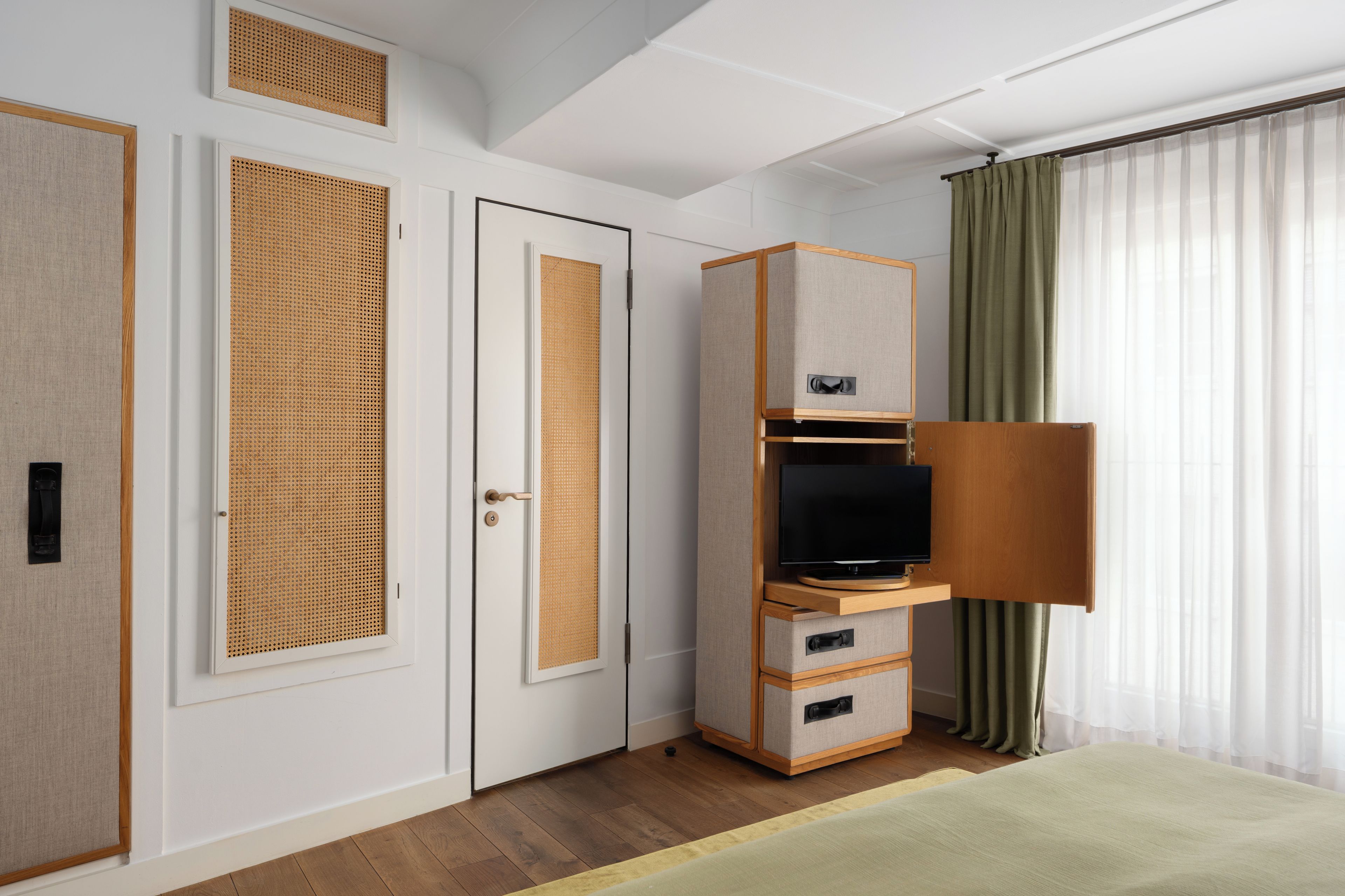 A hotel room with a wooden wardrobe, a television on a wooden stand, and a green curtain.