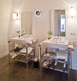 Two sinks with handheld showerheads and a glass shelf for towels.