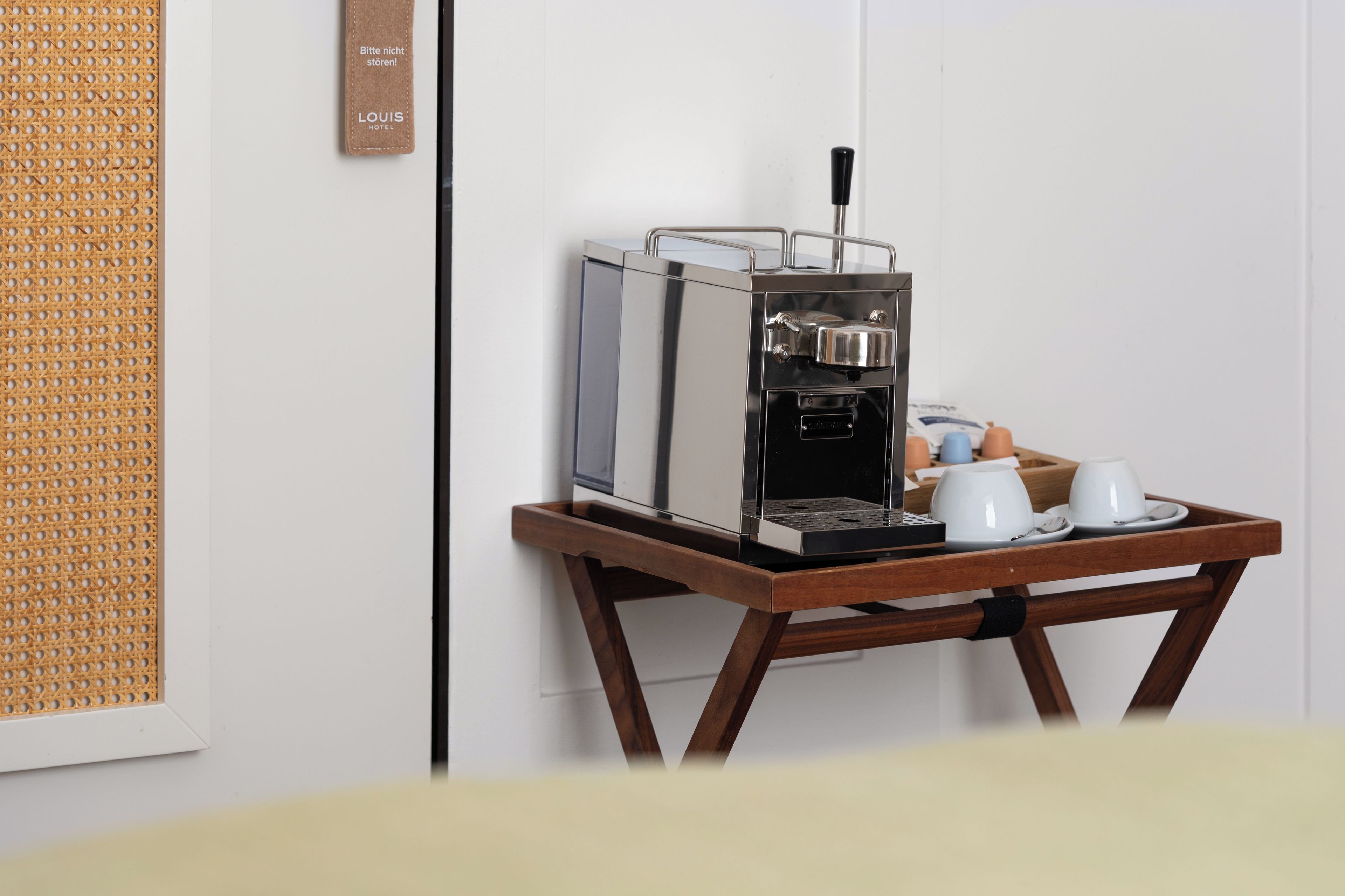 Eine kompakte Kaffeemaschine auf einem Holztisch mit zwei weißen Tassen und einer Eierplatte.