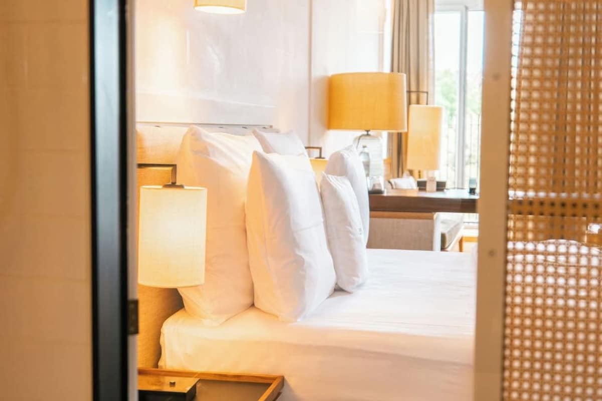 Quarto de hotel com cama, abajures, mesa de cabeceira e janela com cortinas.