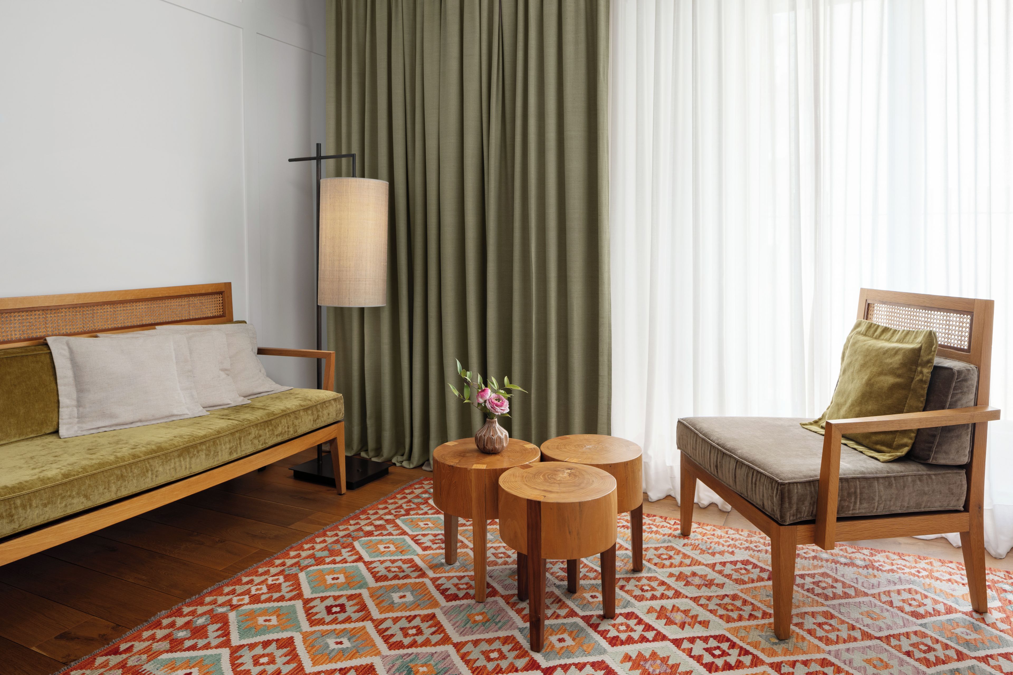 Una habitación con un sofá, una silla, una mesita con un florero y una alfombra estampada.