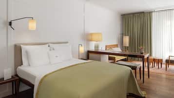 A hotel room with a bed, bedside table, desk, chair, and a view of a curtain.