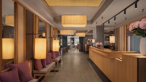 Un hall de hotel con mostrador de recepción, zona de estar con bancos acolchados y grandes lámparas colgantes.