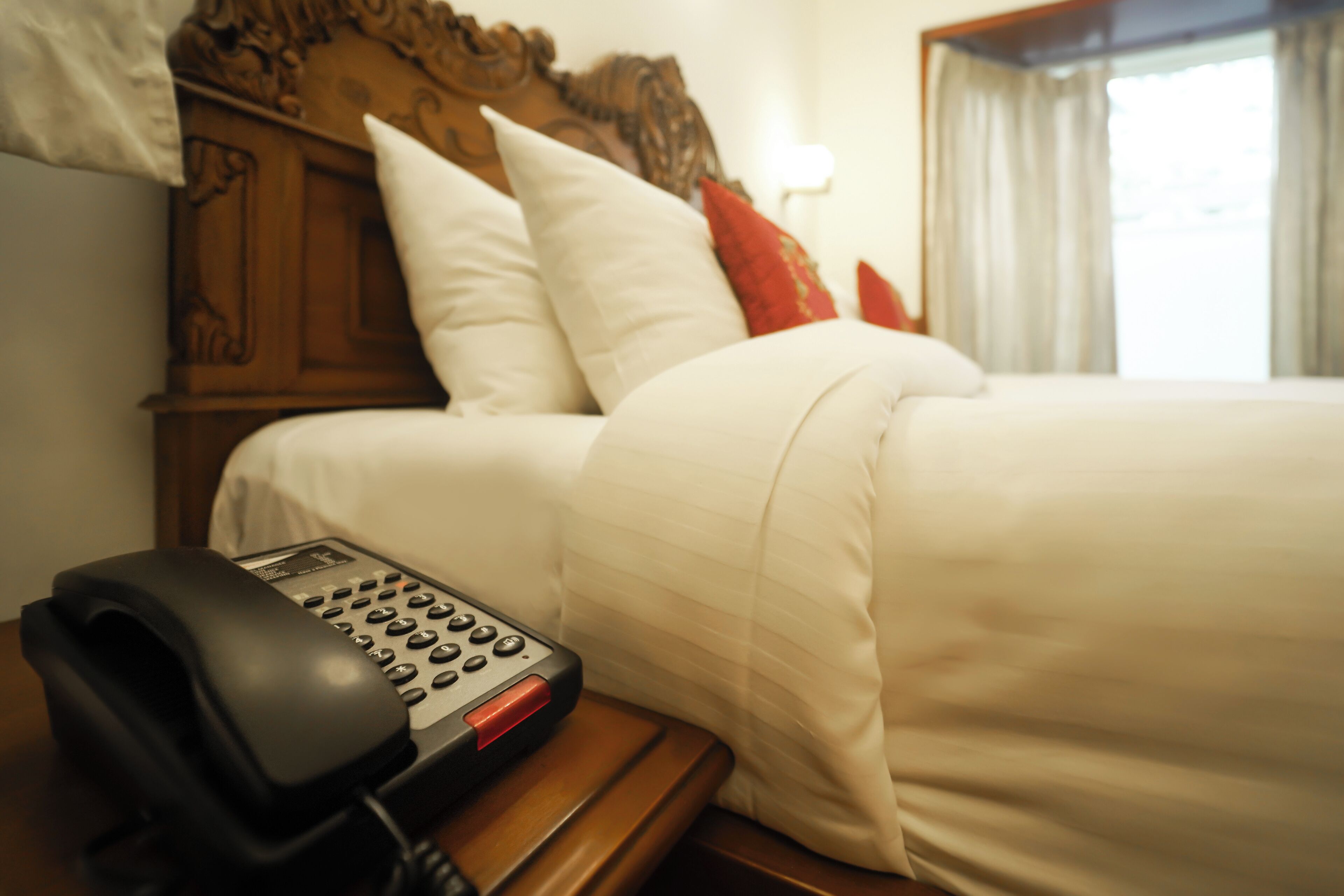 A hotel room with a bed, a wooden headboard, a telephone, and a window with curtains.