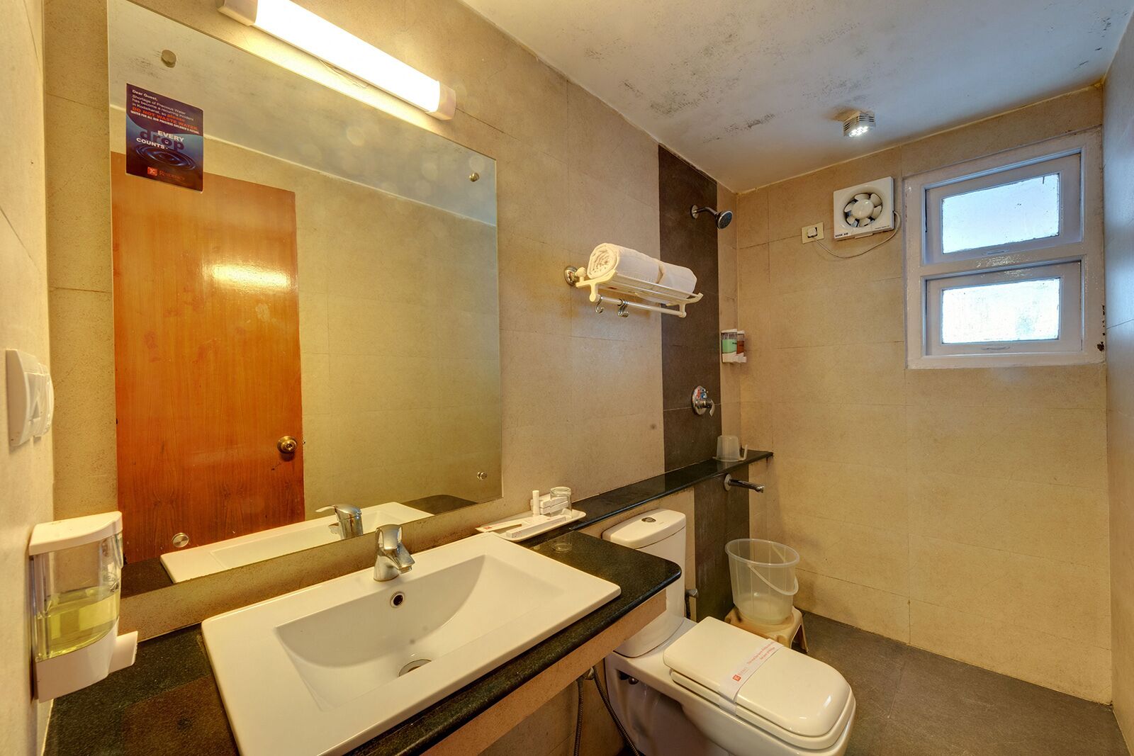 A bathroom with a double sink, a mirror, a towel rack, a toilet, and a window.