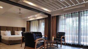 Habitación de hotel con cama, dos sillones de cuero negro, una mesita y un ventanal con cortinas.